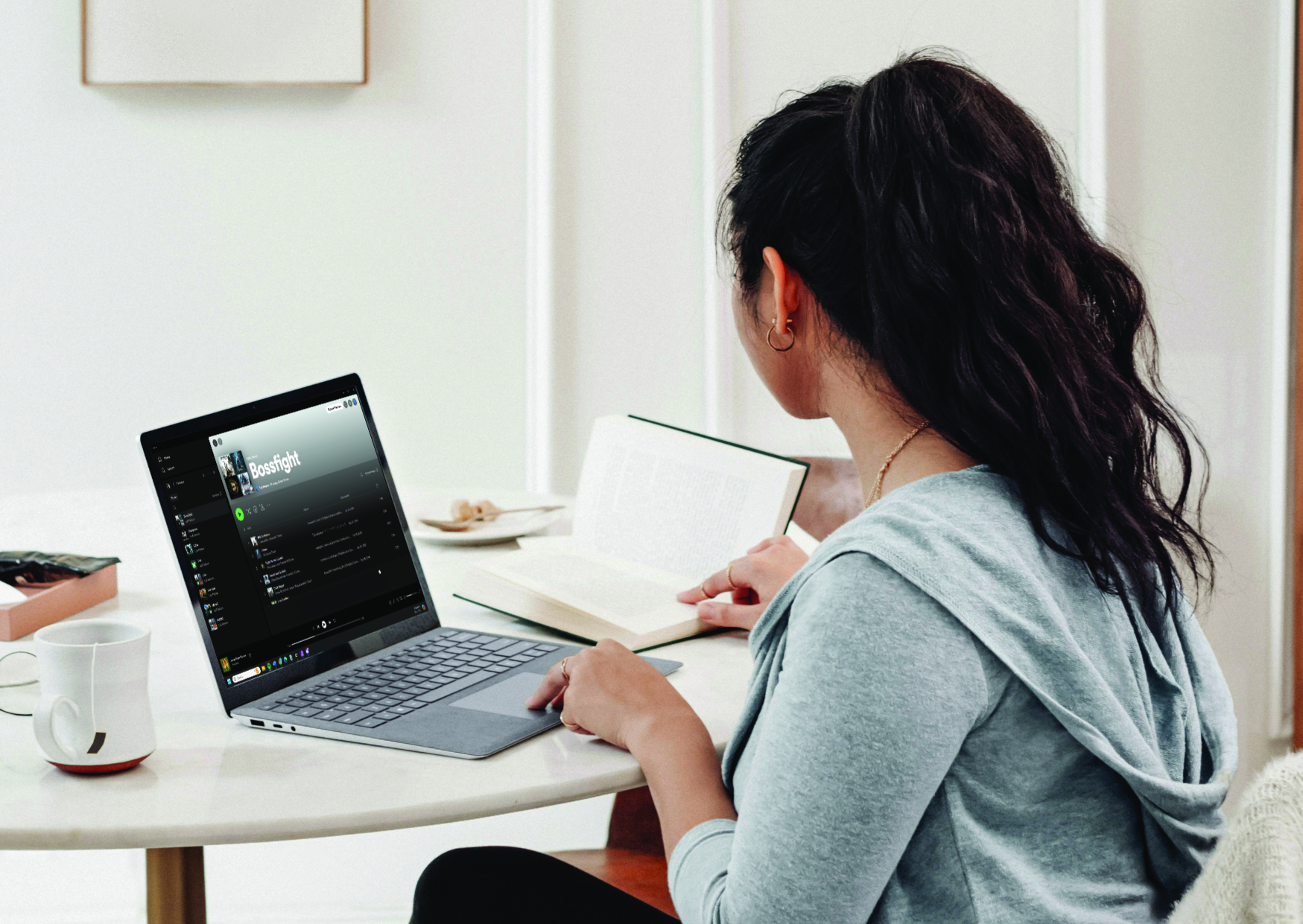 A woman sits at a desk and assembles a music playlist for a bossfight on her laptop.