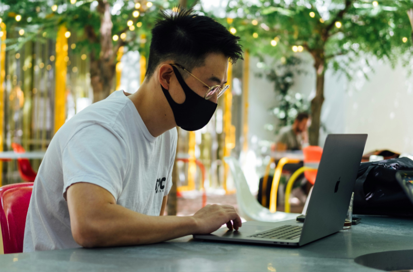 A man sits at a table outside, working on his laptop.
