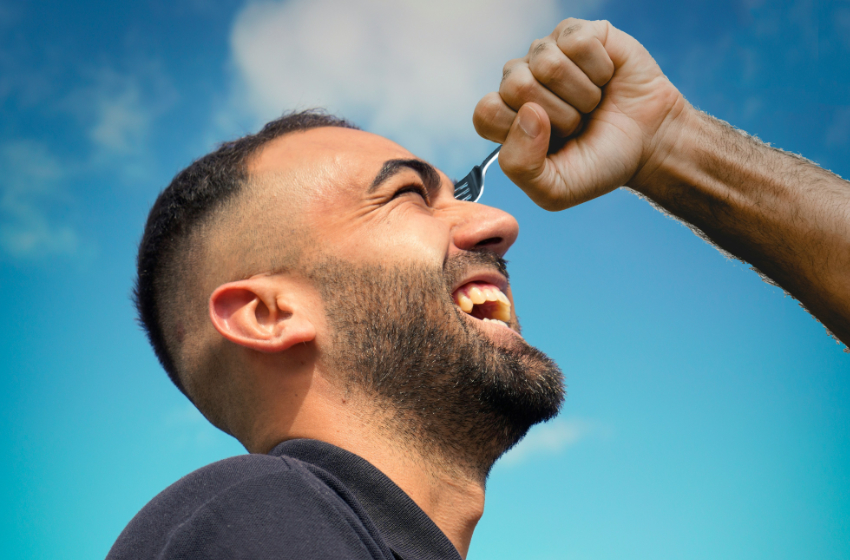 A man laughs as he sticks a fork in his left eye.