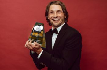 A man in a suit holds up an Ennie award trophy.